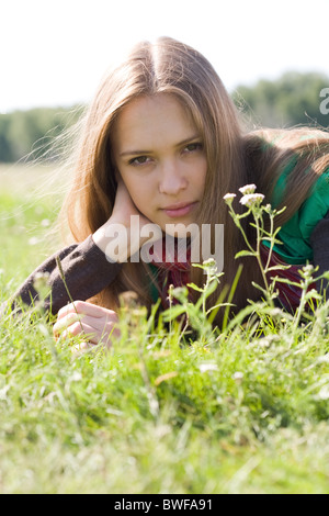 Portrait of attractive young female lying on green grass and looking at camera Stock Photo