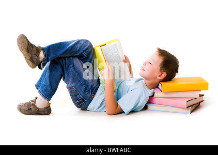 Image of schoolboy lying with his head on the heap of books and reading one of them Stock Photo