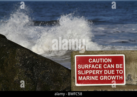 Rough sea and danger warning sign on jetty at Staithes in North Yorkshire. Stock Photo