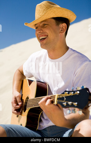 Portrait of handsome man in cowboy hat playing the guitar and singing something on sunny day Stock Photo