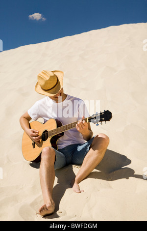 Portrait of happy man in cowboy hat playing the guitar on sandy beach Stock Photo