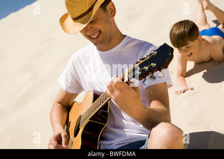 Portrait of happy man in cowboy hat playing the guitar with his son at background Stock Photo
