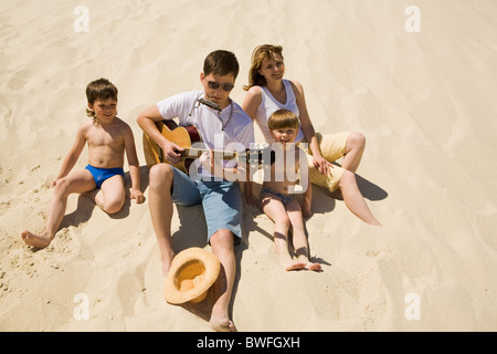 Image of cheerful man playing the guitar with his sons and wife near by Stock Photo