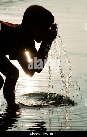 Indian boy drinking water and washing in a lake in India at sunset. Silhouette. Andhra Pradesh, India Stock Photo