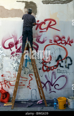Man painting over graffiti on a wall with a paint roller Stock Photo ...