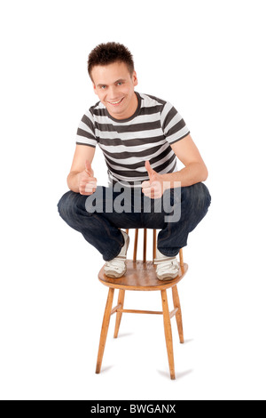 Smiling handsome young man sitting on chair gesturing ok sign isolated against white background Stock Photo