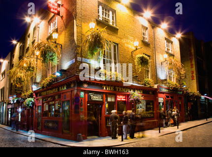 Ireland County Dublin City Temple Bar Pub illuminated at night with people walking past on the cobbled streets Stock Photo