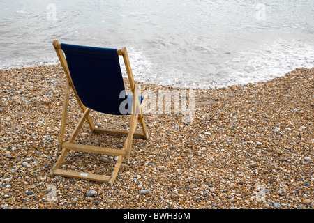 England West Sussex Bognor Regis Single dark blue deck chair on pebble shingle beach looking out to sea with gentle waves Stock Photo