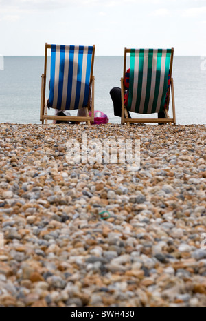 England, West Sussex, Bognor Regis, Two elderly seniors sitting on deck chairs on the pebble shingle beach looking out to sea.