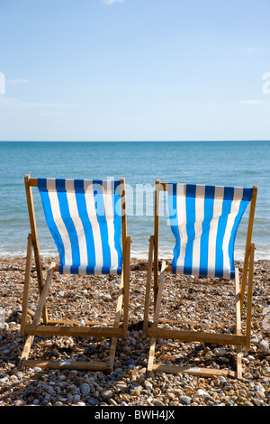 England, West Sussex, Bognor Regis, Two blue and white deck chairs on the shingle pebble beach looking out to sea.