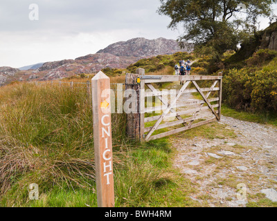 Footpath sign and open farm gate with people walking up on route to Cnicht mountain in Snowdonia National Park from Croesor Gwynedd North Wales UK Stock Photo