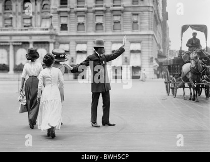 Vintage photo c1911 of a traffic cop in New York City halting a horse-drawn wagon to allow three women to cross the road safely. Stock Photo