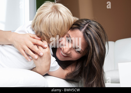 Mother hugging son on couch at home Stock Photo