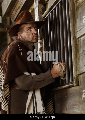 License and prints at MaximImages.com - Cowboy standing at a door in outside of a bank building at night Wild west villain notorious criminal robber Stock Photo