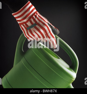 Hand wearing a garden glove holding a watering can Stock Photo