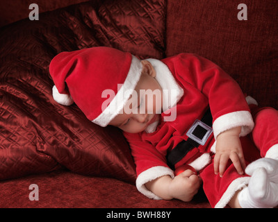 License available at MaximImages.com - Six month old baby boy in Santa costume sleeping on a sofa with a Christmas bauble in his hand Stock Photo