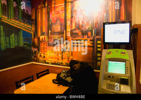 USA New York NYC Manhattan Man asleep at table beneath wall painting of Manhattan beside an ATM cash machine in Macdonald's Stock Photo