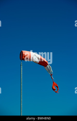 Tattered red and white windsock in light breeze against plain blue sky. Stock Photo