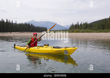 Young woman in kayak, paddling, kayaking, clear, shallow water of upper Liard River, Pelly Mountains behind, Yukon Territory Stock Photo