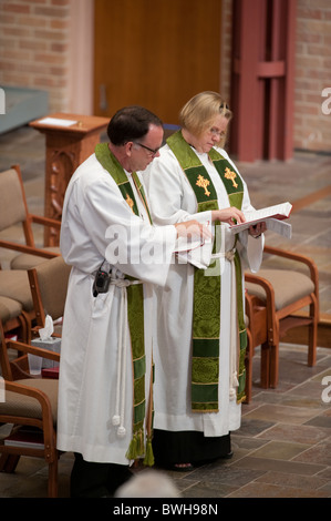 Anglo male presiding minister and Anglo female assisting minister look at their prayer books during Sunday church service Stock Photo