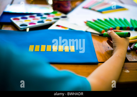 Young child holding a crayon about to write on his pencil case stationary paint pencils and crayons in background Stock Photo
