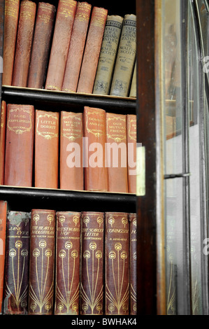 An opened  glassed door bookcase with old editions of classic novels. Stock Photo
