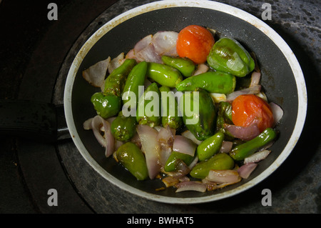 Cooking small sweet green peppers,red onion and small tomatoes in a frying pan with olive oil. Stock Photo