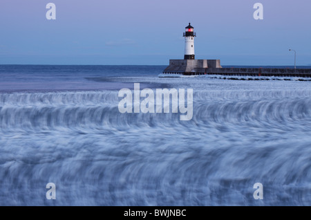 Winter view of lighthouse at dusk in Duluth, MN showing ice floes rolling on waves - slow shutter speed used to reveal motion. Stock Photo