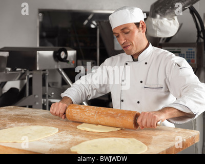 Baker rolling out dough with a rolling pin in a bakery Stock Photo
