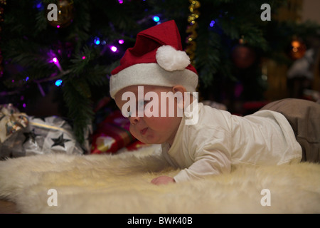 Little baby boy dressed up like santa claus in front of a christmas tree with gifts. Stock Photo