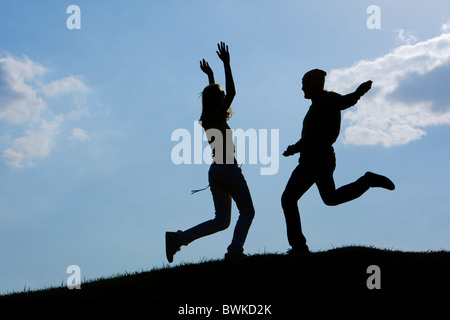 Image of cheerful girl and guy moving energetically against bright blue sky outdoors Stock Photo