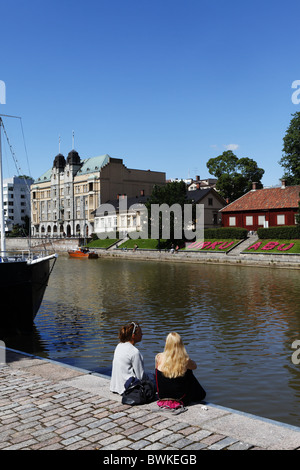 Two young women sitting on the banks of the Aurajoki river, Turku, Finland Stock Photo
