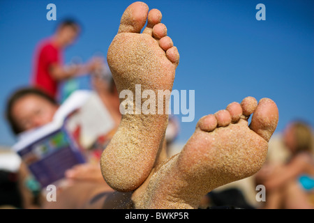 Sandy feet on the beach.  woman relaxes with book on holiday with friends Stock Photo