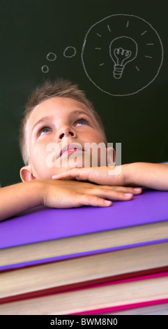 Face of diligent schoolboy looking upwards with his head on stack of books over black background Stock Photo