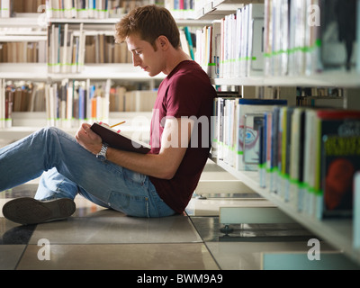 male college student sitting on floor in library, reading book. Horizontal shape, side view, three quarter length, copy space Stock Photo