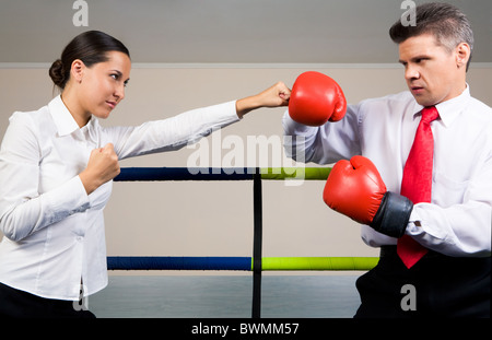 Portrait of aggressive businessman in boxing gloves fighting with serious female Stock Photo