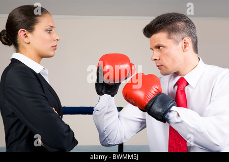 Portrait of aggressive businessman in boxing gloves fighting with serious crossed armed female Stock Photo