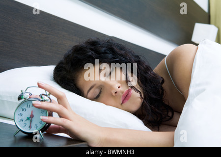 Image of female keeping her hand on top of alarm clock after awakening in the morning