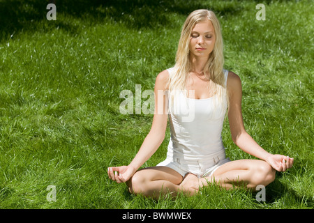 Image of meditating girl seated in pose of lotus on green grass Stock Photo