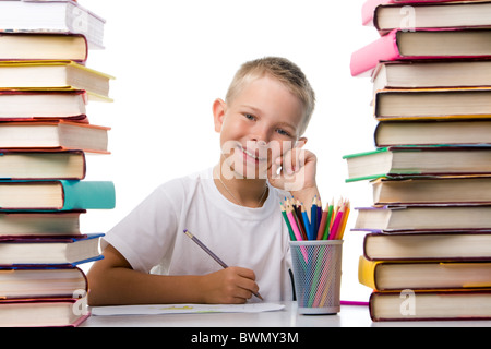 Portrait of cute youngster sitting among stacks of literature and smiling at camera while drawing Stock Photo