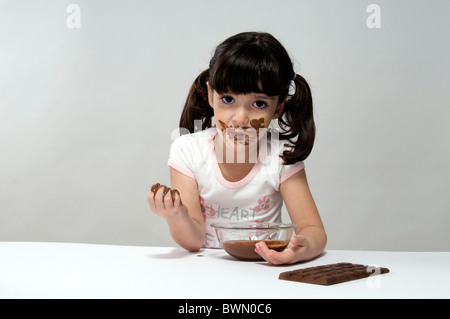 Girl with a pot full of melted chocolate, and a chocolate bar on the table Stock Photo