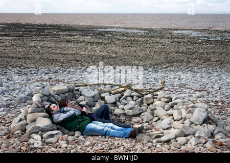 Couple lying down behind stones to keep out of the wind on a walk between Lilstock to Kilve in North Somerset.  DAVID MANSELL Stock Photo