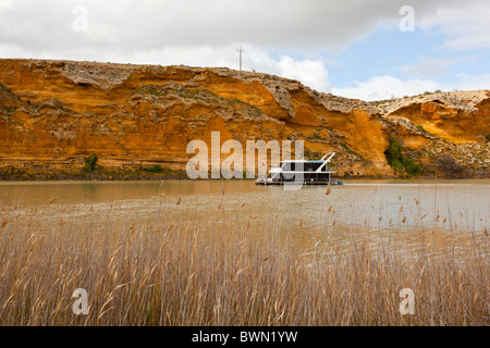 Houseboat cruising past golden cliffs on the Murray River at Walker Flat near Mannum in South Australia