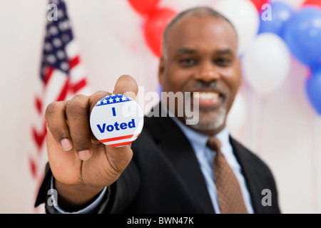 USA, Illinois, Metamora, Portrait of smiling man holding vote button, US flag and balloons in background Stock Photo