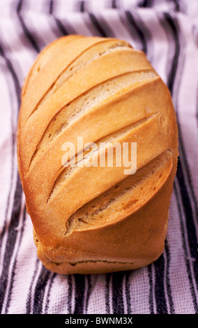A freshly baked loaf of crusty sourdough bread rests on a stripy tea towel. Stock Photo
