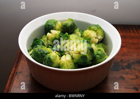 white bowl of cooked brussel sprouts on the end of a wooden table Stock Photo