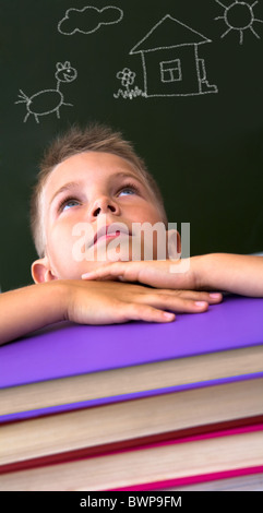 Face of diligent schoolboy looking upwards with his head on stack of books over black background with pictures on it Stock Photo