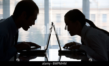 Profiles of man and woman typing on laptops in office Stock Photo