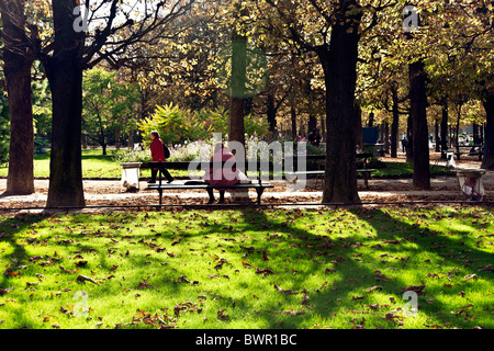 Parisian people enjoying dappled sunlight on autumn foliage flowers & grass on sunny autumn day  in Luxembourg gardens Paris Stock Photo