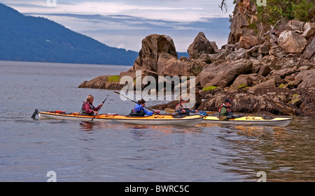 This editorial stock image shows two couples in sea kayaks paddling along the rocky shore in the Pacific Northwest waters. Stock Photo